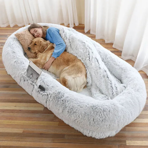 Woman hugging a dog in a fluffy pet bed on a wooden floor.